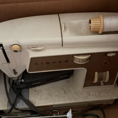 Sale Photo Thumbnail #41: Vintage Singer sewing machine in off-white casing with brown accent panel, featuring original power cord and thread spool.