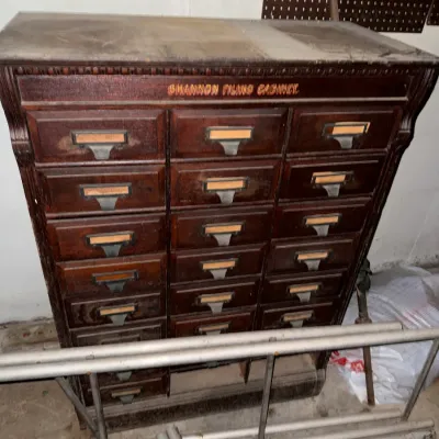 Sale Photo Thumbnail #40: Antique Shannon Filing Cabinet crafted in dark wood with multiple card-catalog-style drawers and original brass label pulls.