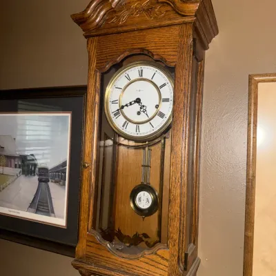 Sale Photo Thumbnail #3: Vintage oak regulator wall clock featuring a carved crown, Roman numeral dial, and visible pendulum enclosed behind glass.