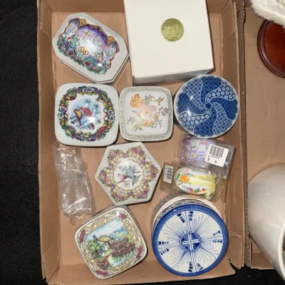 Sale Photo Thumbnail #13: Collection of decorative porcelain trinket boxes featuring floral, bird, and blue-and-white patterns, organized in a cardboard tray.