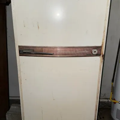 Sale Photo Thumbnail #39: Vintage International Harvester refrigerator, featuring a white enamel finish with copper-toned trim and original emblem, showing light surface wear.