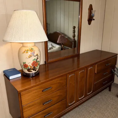 Sale Photo Thumbnail #50: Mid-century modern style wooden triple dresser with matching framed wall mirror. Features a ceramic lamp with floral and bird motifs sitting on top.