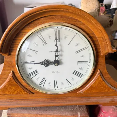 Sale Photo Thumbnail #23: Howard Miller wooden mantel clock featuring a brass bezel, white face with Roman numerals, and ornate black hands.