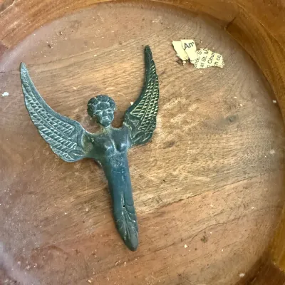 Sale Photo Thumbnail #57: Vintage dark metal winged angel or goddess ornament resting inside a round wooden bowl.