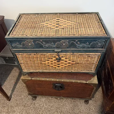 Sale Photo Thumbnail #29: Rustic woven wicker trunk with a carved wooden frame featuring floral details, stacked atop a faux-crocodile leather chest with brass stud hardware and claw feet.