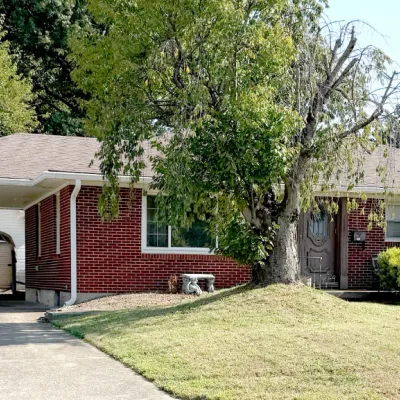 Sale Photo Thumbnail #16: Single-story red brick ranch house featuring an attached carport, front lawn, and mature trees.