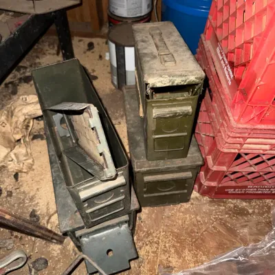 Sale Photo Thumbnail #44: Collection of military surplus metal ammo cans in olive drab, showing dust, wear, and surface rust from storage.