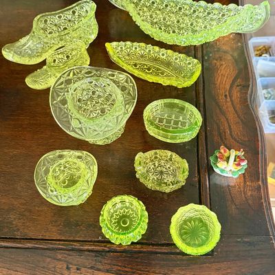 Sale Photo Thumbnail #38: Vaseline vintage press glass., also known as uranium glass. The yellow vaseline is more rare than clear pressed glass. Items shown include decorative shoes, top hat toothpick holder, and salts
