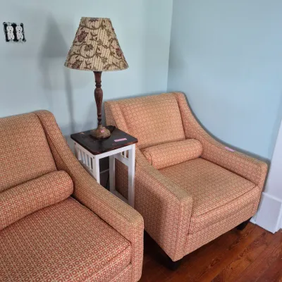 Sale Photo Thumbnail #50: Pair of modern upholstered armchairs with matching bolster pillows, paired with a small two-tone side table and a floral pattern table lamp.