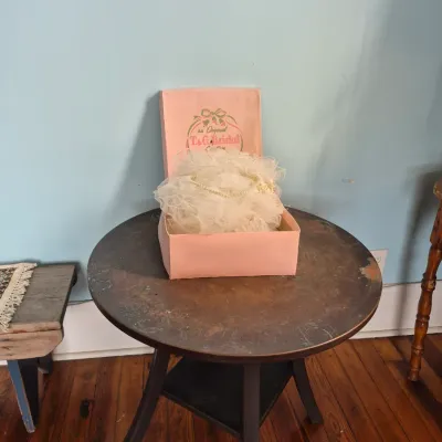 Sale Photo Thumbnail #70: Vintage T & G Bridal Creation headpiece with net tulle and faux pearl details, presented in its original pink box atop a round dark wood accent table.