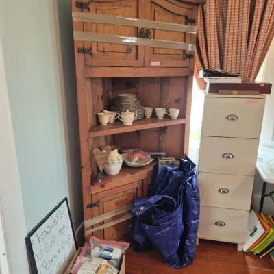 Sale Photo Thumbnail #35: Rustic pine wooden corner cabinet displaying ceramic dishware, positioned next to a cream-colored four-drawer metal filing cabinet.