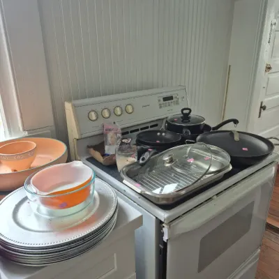 Sale Photo Thumbnail #21: Collection of kitchen items including cookware, Pyrex mixing bowls, and charger plates arranged on and next to a white Magic Chef electric stove.