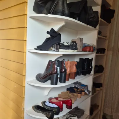 Sale Photo Thumbnail #102: A variety of women's shoes and boots, including heeled ankle boots, flats, and sandals, arranged on a white open shelving unit.