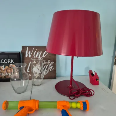 Sale Photo Thumbnail #111: Modern red metal table lamp sitting alongside glass vessels, decorative signs, and a toy foam ball launcher on a table.