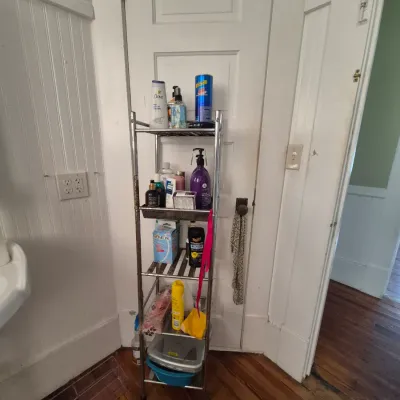 Sale Photo Thumbnail #94: Four-tier chrome wire utility shelving unit holding various personal care and household items.
