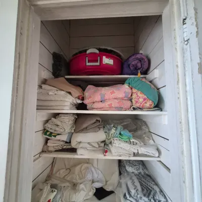 Sale Photo Thumbnail #90: Storage closet packed with assorted household linens, blankets, pillows, and a pink plastic wreath storage box.