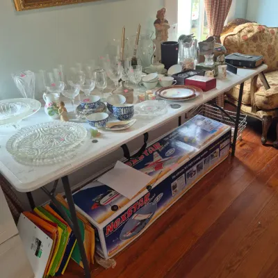 Sale Photo Thumbnail #39: Display table of glassware, china, stemware, and small decor, with a large Hobbico NexSTAR R/C trainer airplane box underneath.