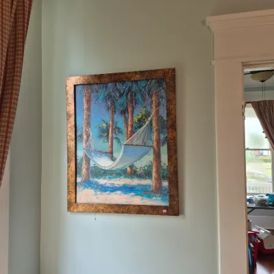 Sale Photo Thumbnail #40: Framed tropical beach oil painting featuring a white hammock strung between palm trees, set in a wide textured bronze-tone frame.