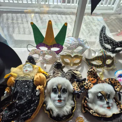 Sale Photo Thumbnail #78: Collection of Mardi Gras and masquerade paraphernalia, including jester-faced wall masks, an ornate porcelain clown doll, and various glittered eye masks.