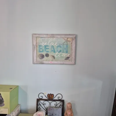 Sale Photo Thumbnail #34: Framed coastal wall art reading 'Relax You're On Beach Time', displayed above decorative home accents including a wrought-iron scroll rack and carved figurine.