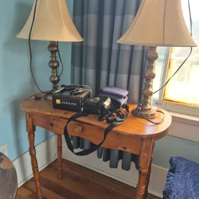 Sale Photo Thumbnail #68: Vintage wooden console table with spindle legs, holding a pair of brass-toned lamps and a Nikon Coolpix digital camera with its original box.