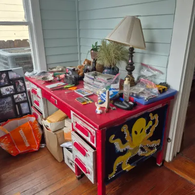 Sale Photo Thumbnail #28: Hand-painted desk featuring a yellow alien octopus motif, trimmed in red and distressed white, topped with assorted household items and a table lamp.