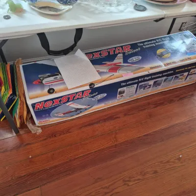 Sale Photo Thumbnail #38: Hobbico NexSTAR Select ready-to-fly R/C model airplane set in its original box, shown beneath a folding table filled with blue-and-white chinaware.