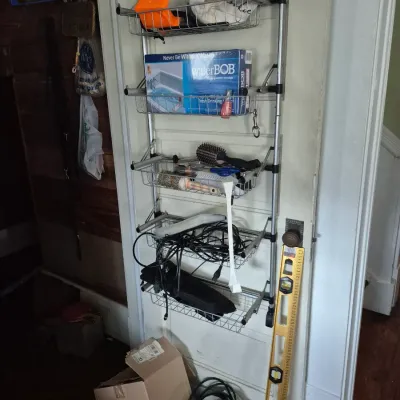 Sale Photo Thumbnail #56: Over-the-door metal rack organizer filled with various household items, including a boxed waterBOB emergency water storage container, hairbrushes, and cords.