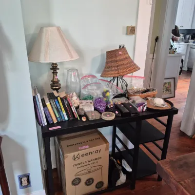 Sale Photo Thumbnail #42: Black console table lined with items including two table lamps, hardcover books, craft supplies, and a boxed Keenray towel warmer underneath.