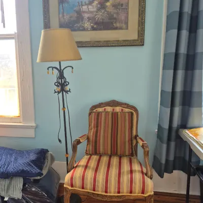 Sale Photo Thumbnail #73: French Provincial style armchair with striped upholstery, paired with an ornate metal floor lamp and a framed coastal landscape print.