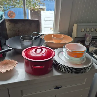 Sale Photo Thumbnail #18: Collection of vintage kitchenware featuring a red enamel covered pot, a stack of silver-tone chargers with Pyrex mixing bowls, and cookware set on a counter.