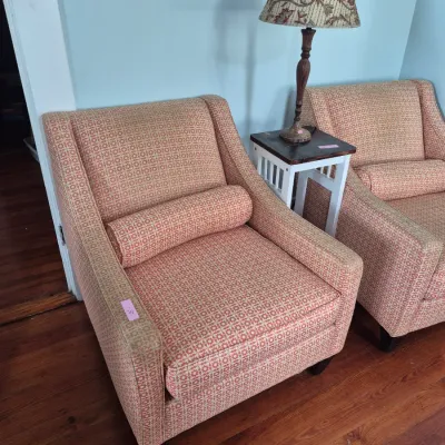 Sale Photo Thumbnail #48: Pair of patterned orange and beige upholstered armchairs with matching bolster pillows, flanked by a small two-tone side table and a floral lampshade.
