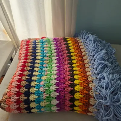 Sale Photo Thumbnail #108: Handmade vintage crochet afghan blanket featuring colorful rainbow stripes and light blue fringe detailing.
