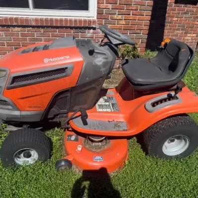 Husqvarna orange riding lawn mower showing wear, including tears on the black padded seat.