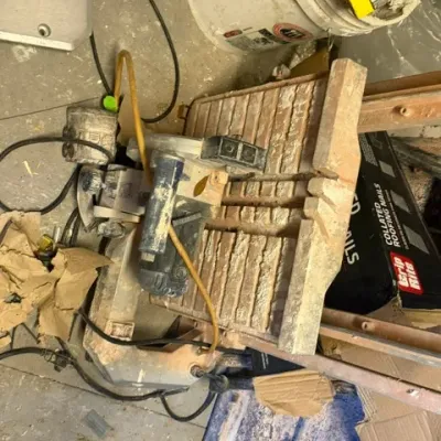 Used sliding compound miter saw covered in construction dust, featuring attached power cords and a water line assembly.