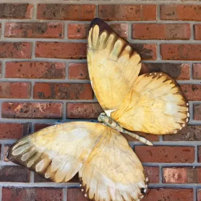 Large vintage butterfly wall sculpture in shades of yellow and brown, mounted on a brick wall.