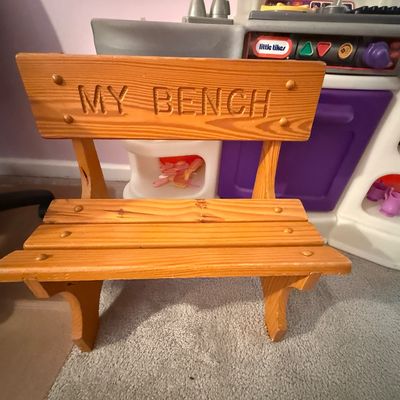 Small wooden child's bench with slatted seat and carved backboard reading "MY BENCH", set in front of a Little Tikes play...