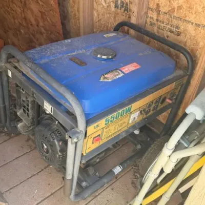 US General 5500W portable gas generator with a blue fuel tank and black steel roll cage, showing wear and dust from storage.