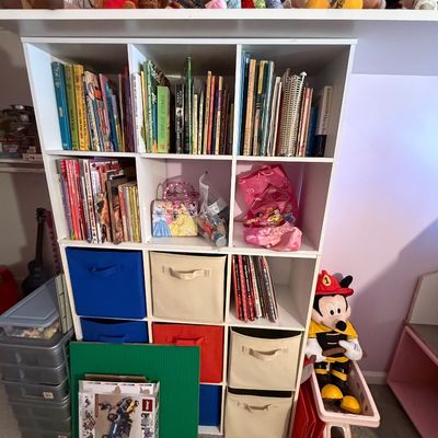White 8-cube laminate organizer shelf filled with children's books, fabric storage bins, toys, and plush animals on top.