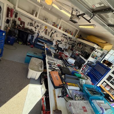 Workshop garage filled with folding tables displaying various hand tools, hardware organizers, toolboxes, and shop equipment.