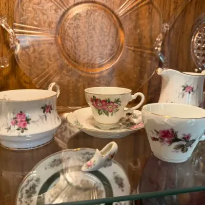 Vintage floral porcelain tea service pieces, including tea cups, saucers, a creamer, sugar bowl, and miniature porcelain shoe, displayed...