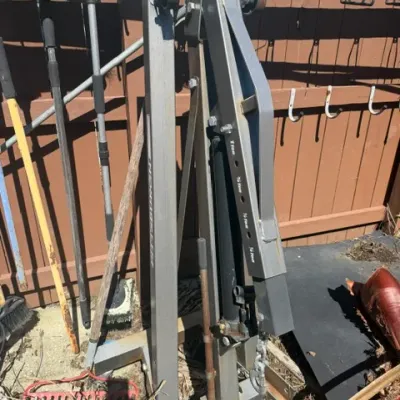 Foldable heavy-duty hydraulic shop crane engine hoist stored vertically near outdoor tools.