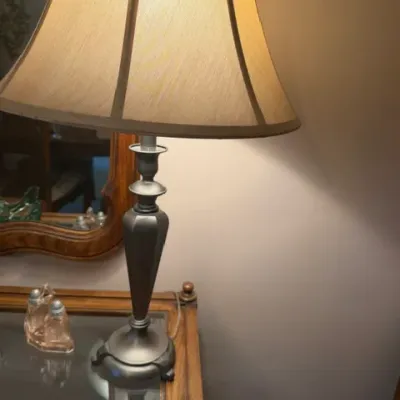 Traditional pewter or dark metal table lamp featuring a flared fabric lampshade and a turned baluster-style body.