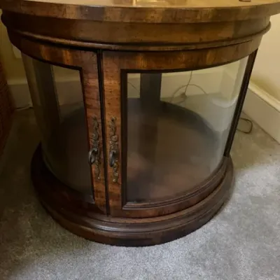 Round traditional burled wood side table featuring curved glass cabinet doors and decorative ornate pulls.
