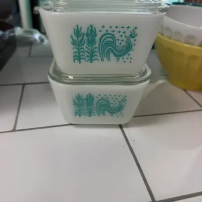 Vintage Pyrex Butterprint pattern refrigerator dishes with clear glass lids, stacked on a countertop.