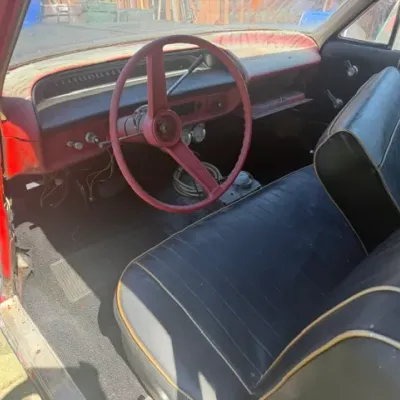 Interior view of a vintage project car featuring a red dashboard, three-spoke steering wheel, and black vinyl bench seating.