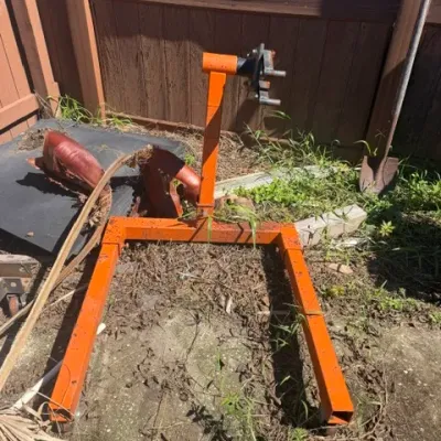 Heavy-duty orange steel engine stand, showing some weather wear and surface rust, placed outdoors.