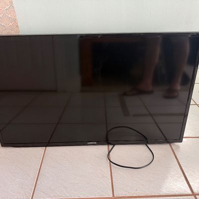 Black Samsung flat-screen LED television resting on tiled floor, complete with attached power cord.