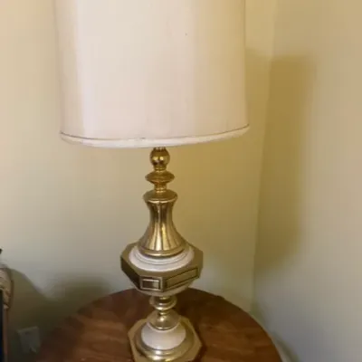 Vintage mid-century brass and cream table lamp with a tall, light cream drum shade, resting on a round wood end table.