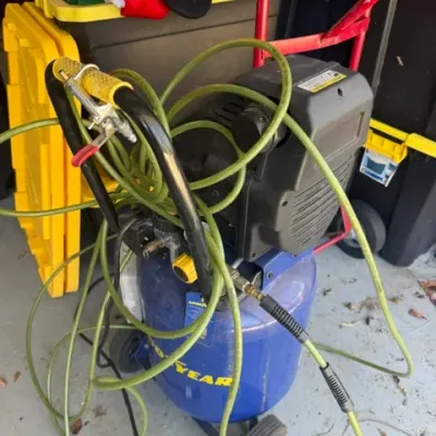 Goodyear portable air compressor with attached green air hose and spray nozzle, showing light cosmetic wear.